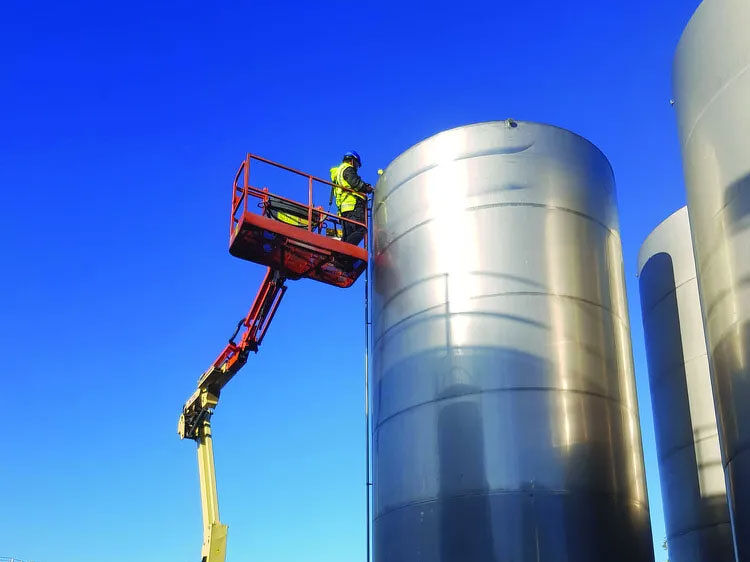 Technician on a scissor lift working on large steel storage tanks
