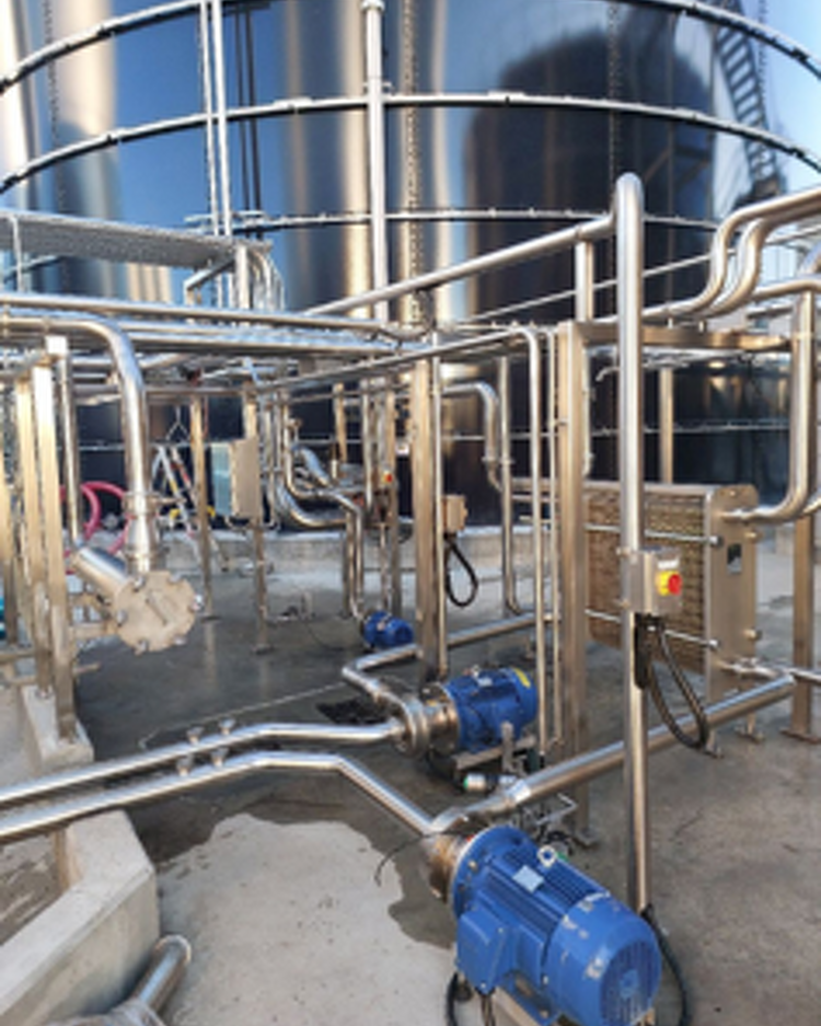 Stainless steel pipework and pumps beside a large storage tank